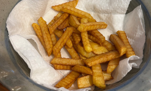 golden homemade french fries draining on paper towels in a bowl after deep frying