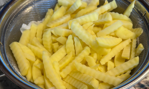 Fresh-cut homemade french fries draining in a colander before deep frying