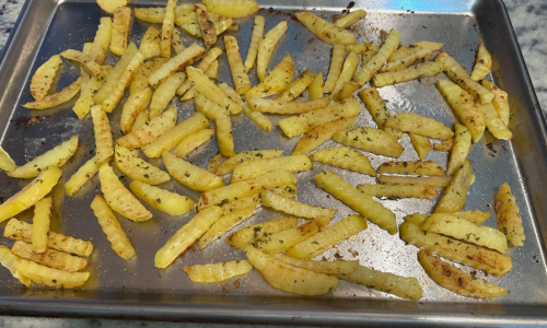 homemade french fries spread on a baking sheet ready for the oven as a safer alternative to deep frying