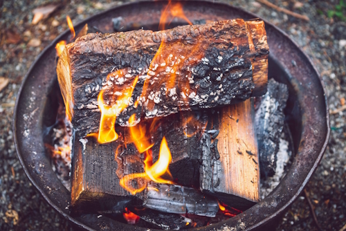 logs burning with orange flames in an outdoor metal fire pit - homestead fire safety