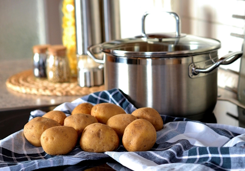 fresh whole potatoes on a blue checkered towel with a stainless steel stockpot in the background